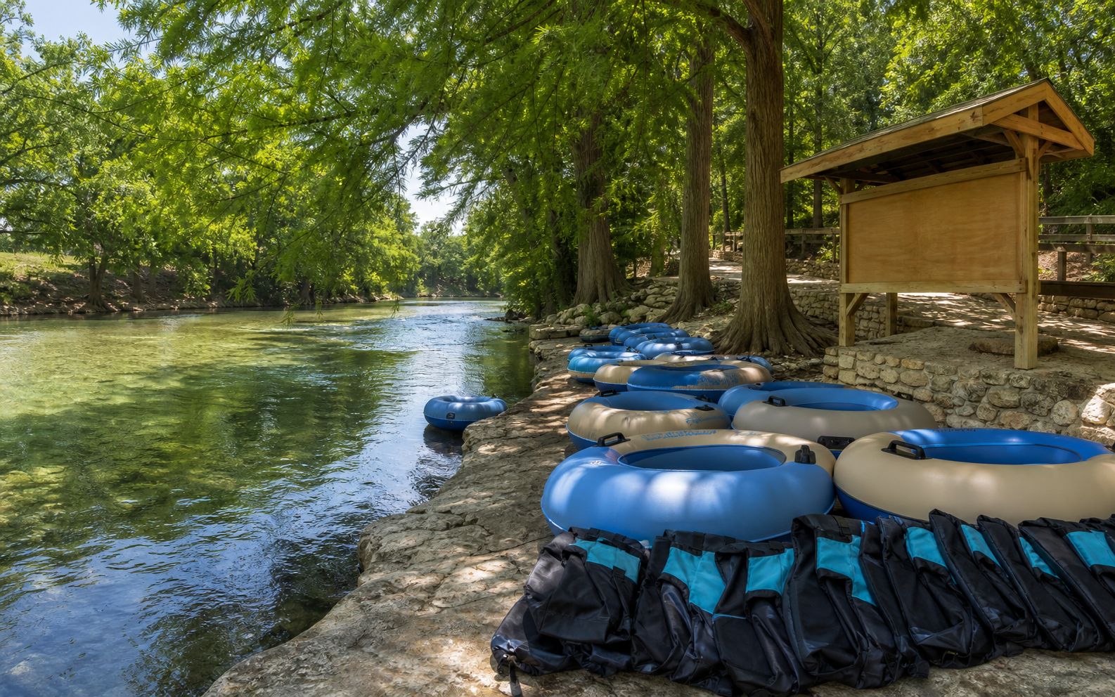 Shaded New Braunfels river put-in with tube floats and safety gear